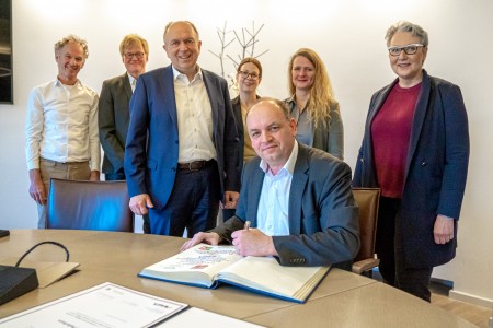Staatssekretär Victor Haase (sitzend) trug sich im Beisein von Michael Rüngeler (Leitung Kreisstraßenbauamt), Martin Lohmann (Ministerium für Umwelt, Naturschutz und Verkehr des Landes Nordrhein-Westfalen), Landrat Christoph Rüther, Linda Noack (Mitarbeiterin Kreisstraßenbauamt), Astrid Butt (OWL GmbH) und Christine Fuchs (AGFS-Vorstand, v.l.) in das Goldene Buche des Kreises Paderborn ein. © Julian Sprenger, Kreis Paderborn Staatssekretär Victor Haase (Ministerium für Umwelt, Naturschutz und Verkehr des Landes Nordrhein-Westfalen,l.) überreicht gemeinsam mit Christine Fuchs (AGFS-Vorstand, r.) die Urkunde an Landrat Christoph Rüther (Mitte). © Julian Sprenger, Kreis Paderborn